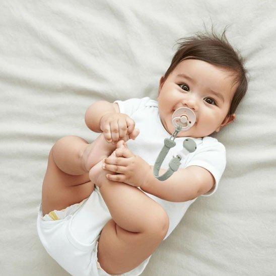 Attache tetine universel et mignon bebe tient ses pieds