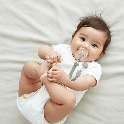 Attache tetine universel et mignon bebe tient ses pieds